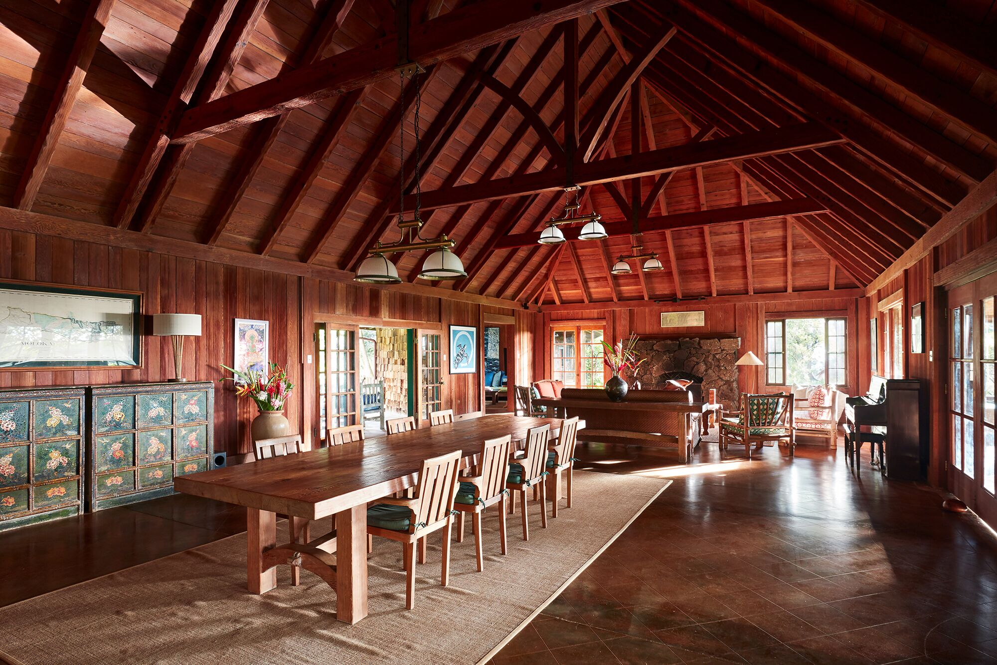 A spacious dining area with a long wooden table and chairs, surrounded by wooden walls and large windows.