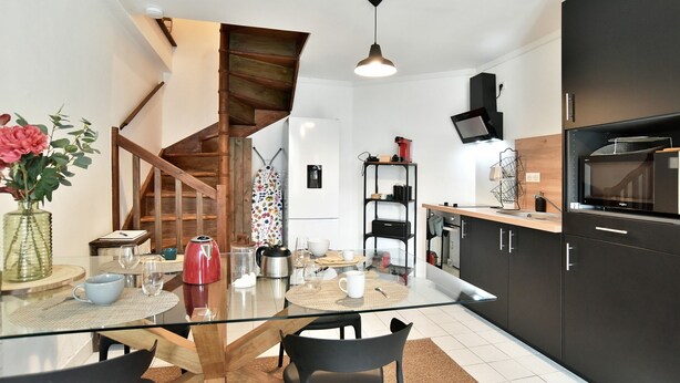 Une cuisine moderne avec une table à manger en verre, des chaises noires et un escalier en bois.