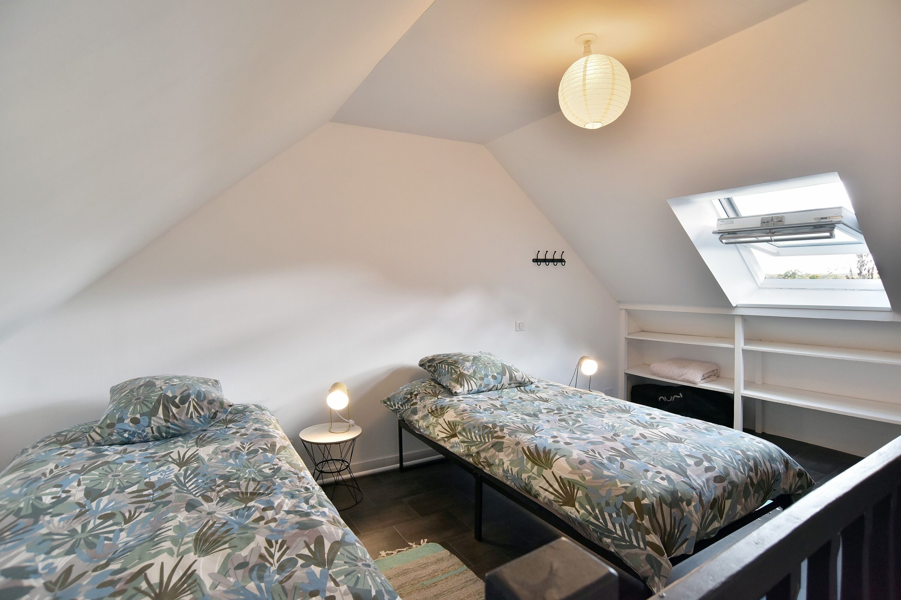 A small, well-lit attic bedroom with two beds, a skylight, and a simple, modern design.
