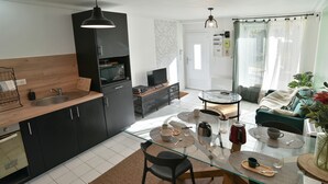 Une cuisine moderne avec un plan de travail en bois, des armoires noires et un four encastré. On y trouve également un coin repas avec une table en verre, des chaises et une machine à café.