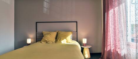 A bedroom with a bed, bedside lamps, and a window with curtains.