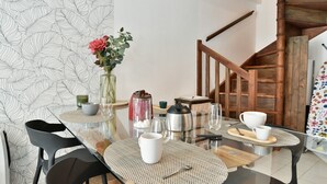 Un coin repas avec une table en verre, des chaises noires, un vase avec des fleurs, une bouilloire et une machine à café.