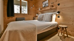Ein gemütliches Schlafzimmer in einer Holzhütte mit einem Bett, einem Nachttisch, einer Lampe und einem Fenster mit Vorhängen.