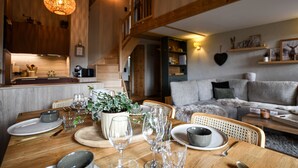 Ein Holzespeisetisch ist gedeckt mit Tellern, Schüsseln und Gläsern, daneben ein Blumentopf und eine Treppe, die zu einer oberen Ebene führt.