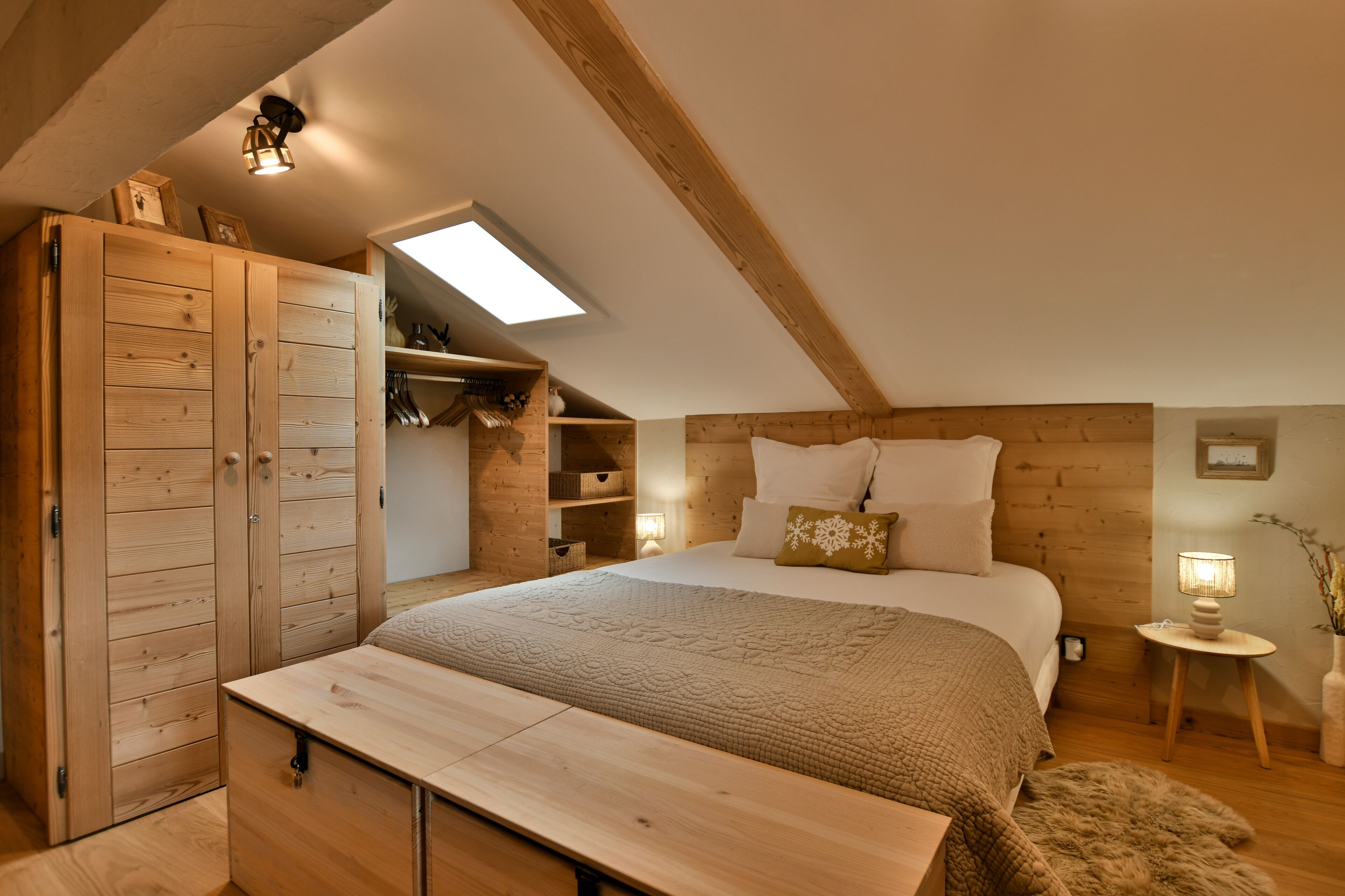 Ein gemütliches Schlafzimmer mit schrägem Dach, Holzschrank, Nachttisch und einer kleinen Nachttischlampe.