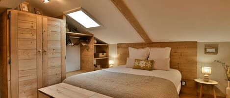 Ein gemütliches Schlafzimmer mit schrägem Dach, Holzschrank, Nachttisch und einer kleinen Nachttischlampe.