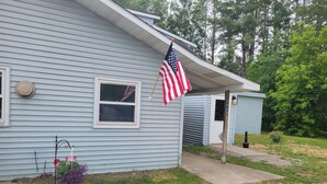 A light blue house with an American flag, a mailbox, and a small shed. - Near lakes/rivers, town, snowmobile trails and access to hunting and state land. (Grayling)