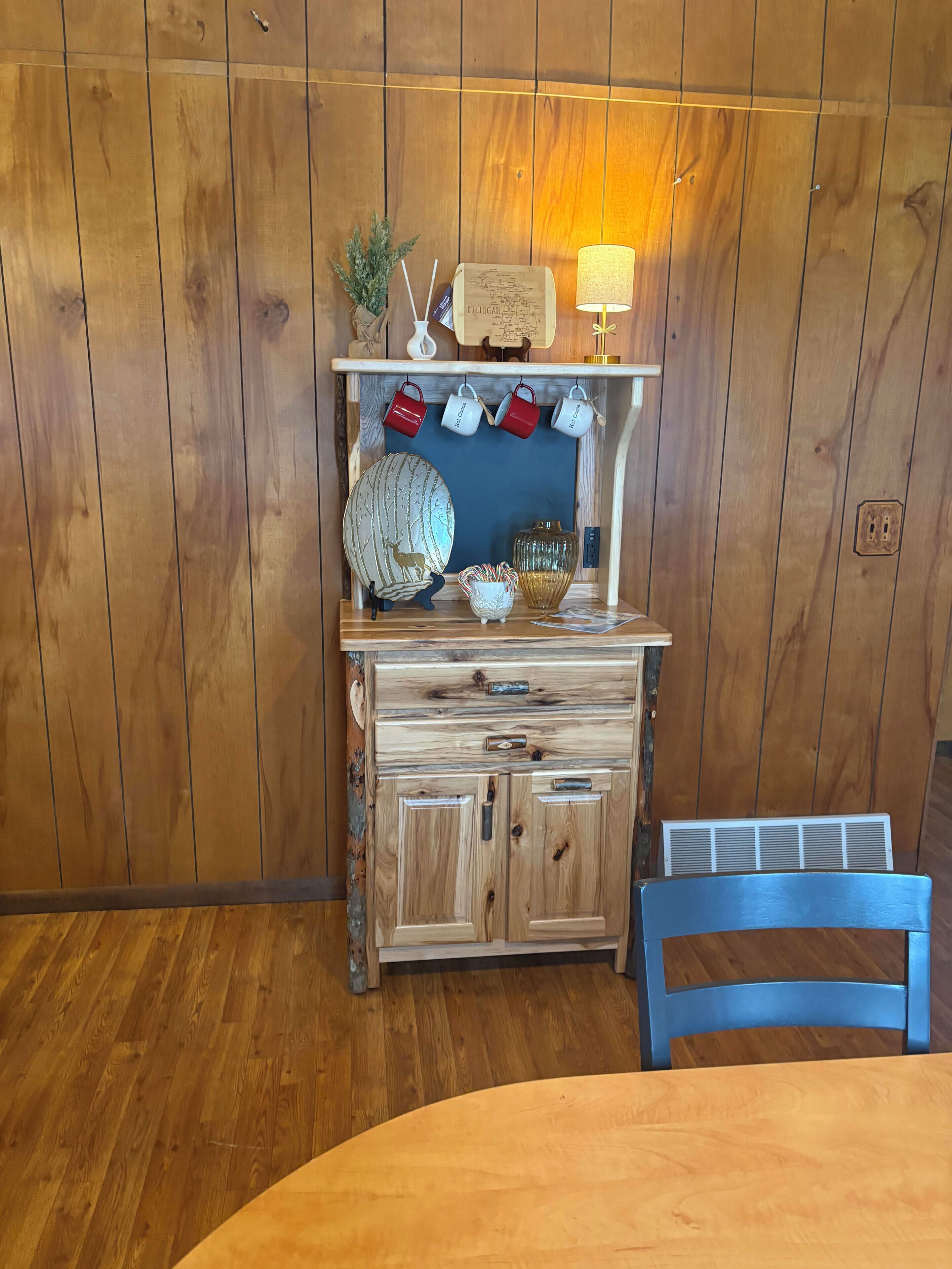 Un mueble de madera con un globo terráqueo, tazas rojas y blancas, y una lámpara.
