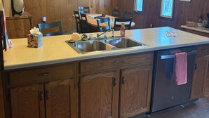 A wooden interior with a kitchen area featuring a large island, wooden cabinets, and pendant lighting. - Near lakes/rivers, town, snowmobile trails and access to hunting and state land. (Grayling)
