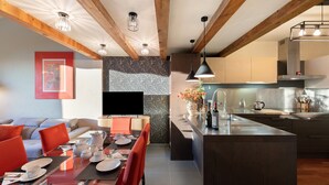 Eine moderne Küche mit Kochinsel, ein Essbereich mit Glastisch und ein Wohnbereich mit Sofa und roten Sesseln.