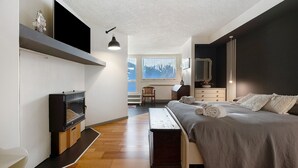 Ein Schlafzimmer mit Bett, Fernseher, Kamin, Fenster und Schreibtisch.