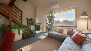 Ein Wohnzimmer mit einer Couch, einem roten Sessel, einer Treppe, einer Pflanze und einem Fenster mit Bergblick.