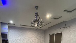 Un salon moderne avec un canapé d’angle, une table basse, un lustre et une grande fenêtre.