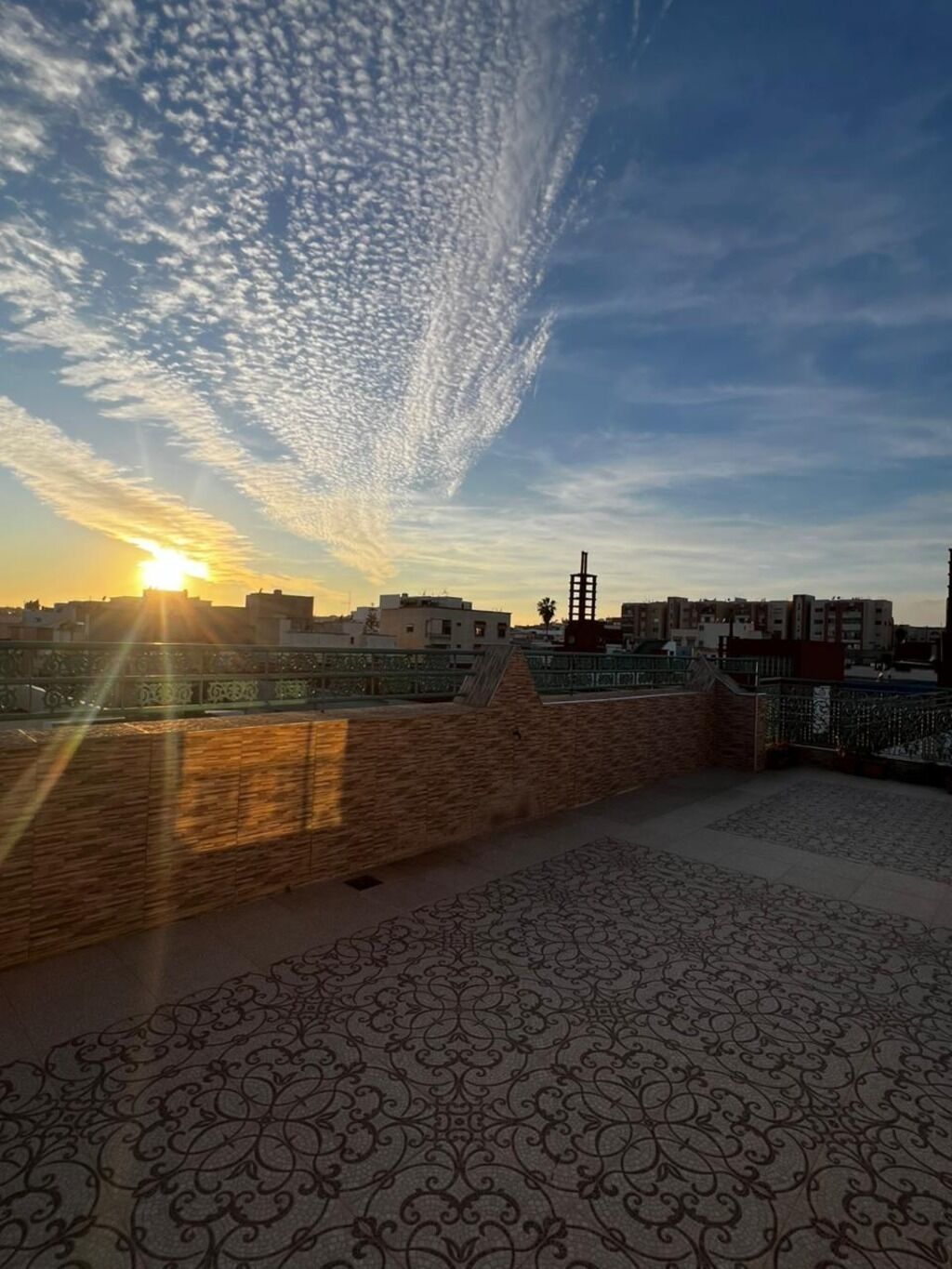 Une terrasse sur le toit, dotée d’un sol à motifs, d’un mur en briques et offrant une vue sur le coucher de soleil au-dessus d’une ville.