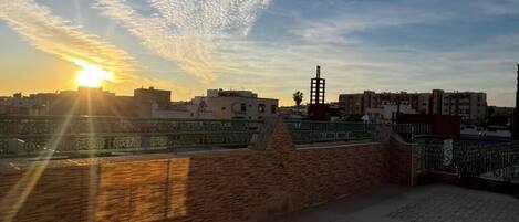 Une terrasse sur le toit, dotée d’un sol à motifs, d’un mur en briques et offrant une vue sur le coucher de soleil au-dessus d’une ville.