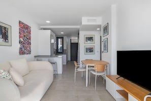 A modern living room with a sofa, a dining table with chairs, a TV, and artwork on the walls.