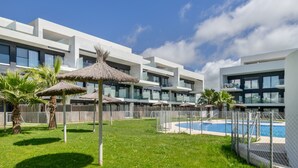 Een modern hotel met een zwembad, parasols en een verzorgd gazon.