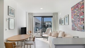 Een moderne woonkamer met een eethoek, een bank, een televisie en een balkon met een glazen deur.
