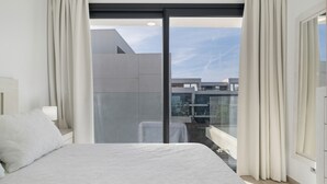 Een slaapkamer met een groot bed, een nachtkastje, een lamp en uitzicht op de stad door een schuifdeur.