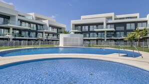 Een modern hotel met een zwembad, meerdere balkons en een heldere lucht.