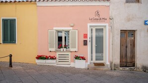 Un edificio con facciata rosa, un portone con l'insegna 'La Casa di Mia' e cassette fiorite con fiori rossi.