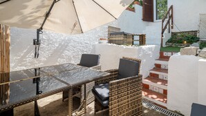 Una veranda esterna con mobili in vimini, un tavolo in vetro e un ombrellone grande.