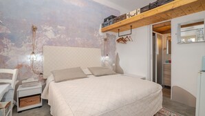 Een slaapkamer met een bed, nachtkastje, wandplank en een deur naar een andere kamer.