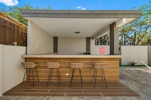 An outdoor bar area with a counter, three wicker bar stools, and a wooden floor. - Prime location • Private pool & BBQ (Noord)