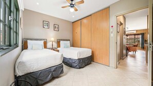Habitació d'hotel amb dos llits, un ventilador de sostre, una finestra i vista a la zona d'estar.