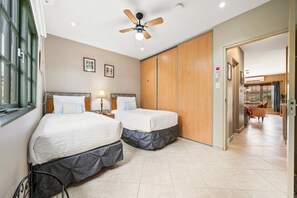 A hotel room with two beds, a ceiling fan, a window, and a view into the living area. - Charming 2 BR Condo with 2 Community pools! (Noord)