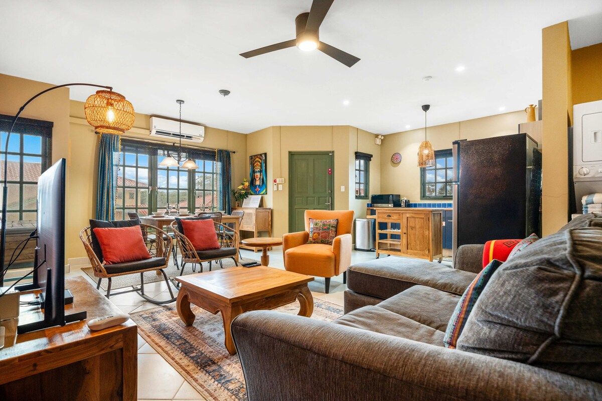 A living room with a sofa, armchairs, a coffee table, a television, and a ceiling fan.