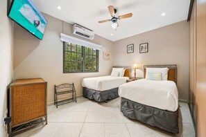 A hotel room with two beds, a ceiling fan, an air conditioning unit, a television, and a window with a view of greenery. - 2BR Condo w/ 2 Community Pools, near Palm Beach (Noord)