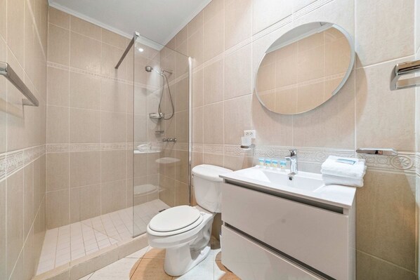 Casa de banho moderna com chuveiro envolto em vidro, sanita e lavatório com espelho acima.