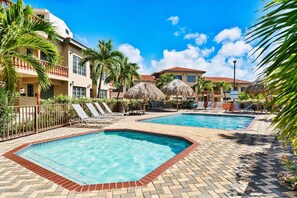 A hotel pool area with two pools, lounge chairs, and palm trees. - Charming 2 BR Condo with 2 Community pools! (Noord)
