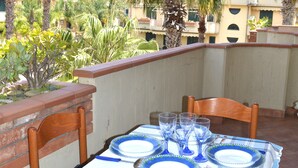 Pátio externo com mesa posta para refeições, rodeado por cadeiras e um toldo listrado por cima.