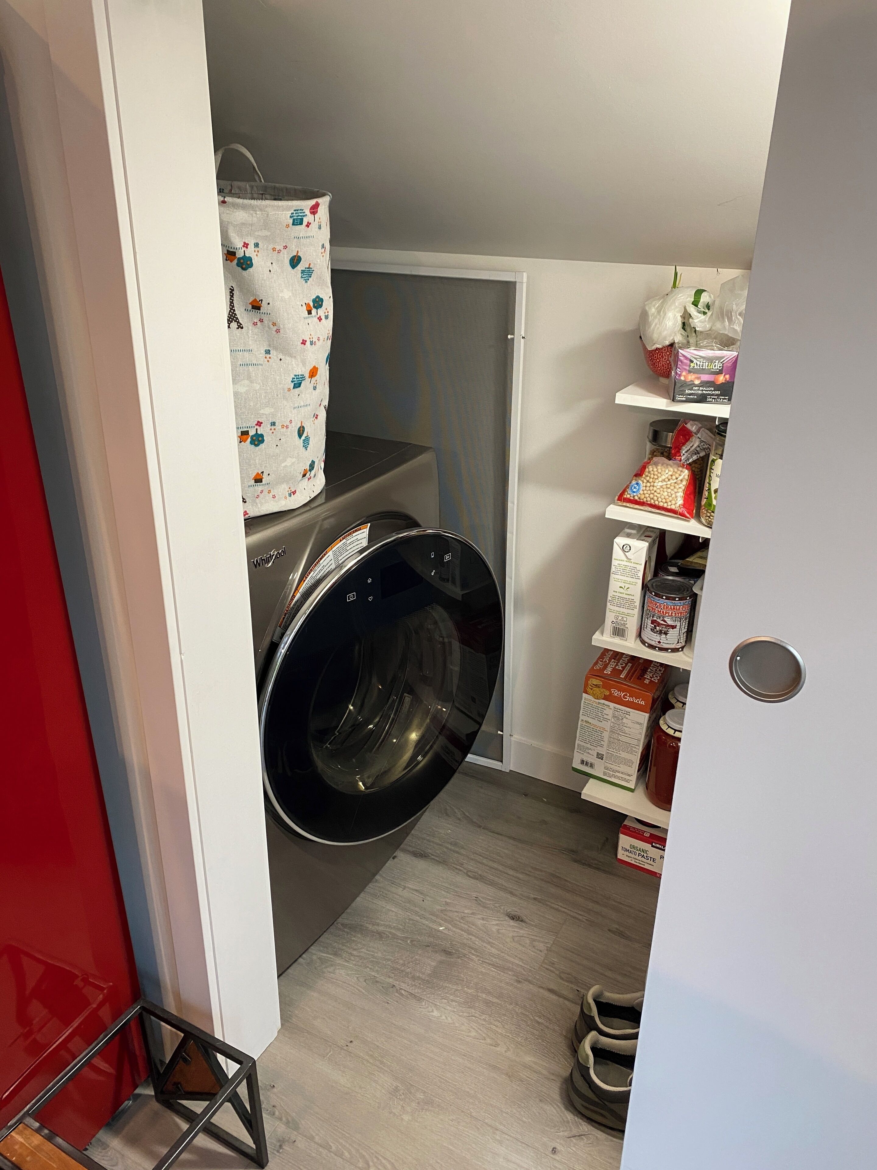 Une buanderie équipée d’un lave-linge à chargement frontal, d’une étagère contenant divers produits alimentaires et d’une chaise rouge.