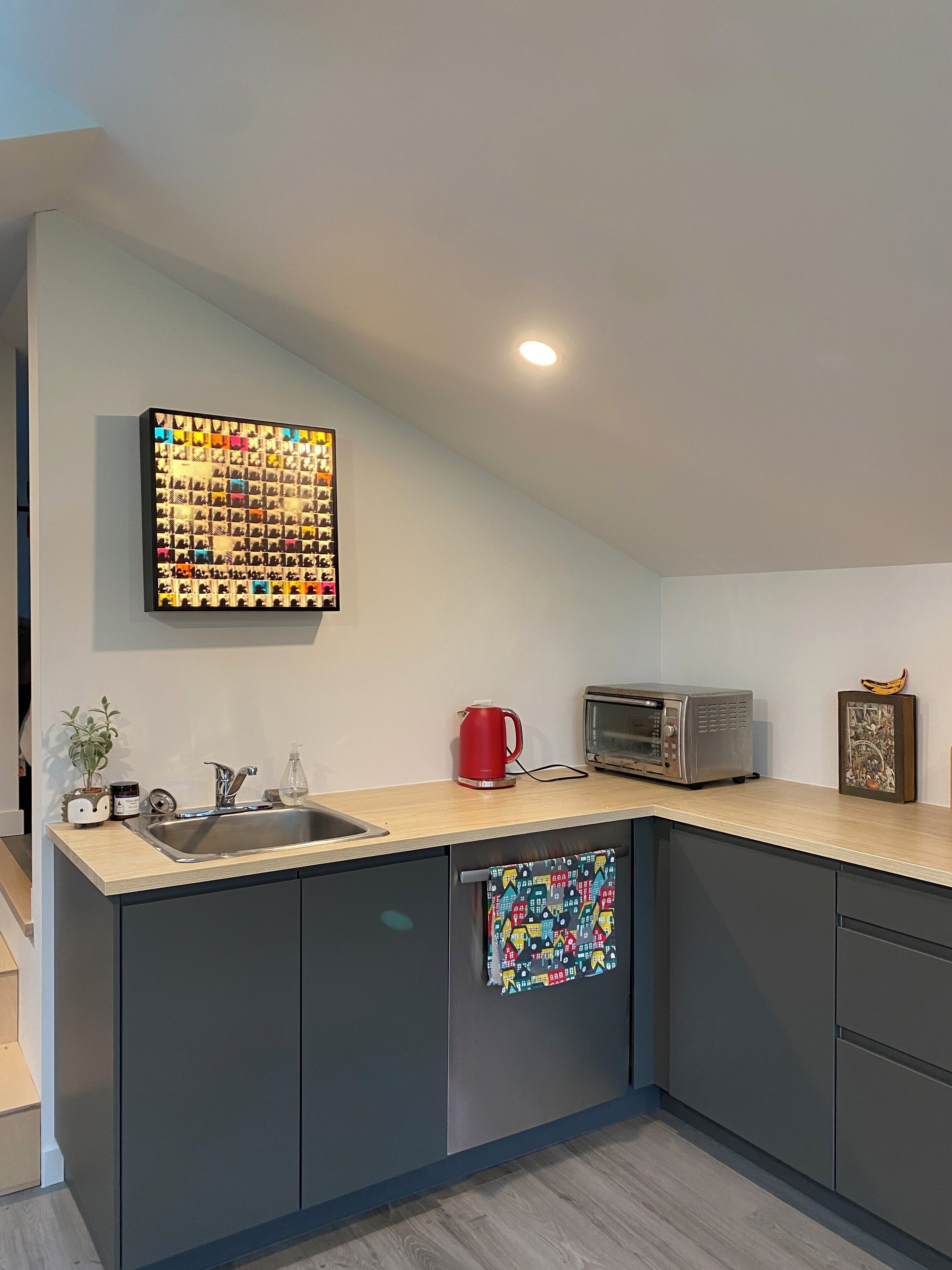 Een moderne keuken met een spoelbak, een rode waterkoker, een broodrooster en een aan de muur bevestigd schilderij.