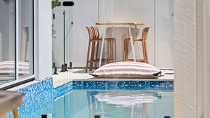 Ett område vid poolen med en inglasad sektion, flätade stolar, ett träbord och en randig kudde.