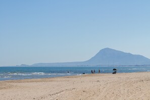 Una playa con una montaña al fondo, algunas personas y un perro.