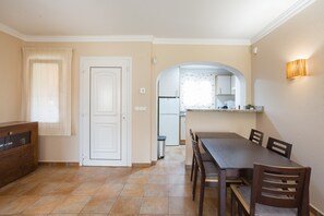 Una cocina con refrigerador, una mesa de comedor con sillas, un mueble y una ventana con cortinas.