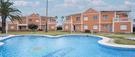 A swimming pool with a curved edge, surrounded by buildings with balconies and a palm tree.