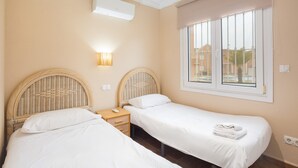 Ein Schlafzimmer mit zwei Einzelbetten, einem Nachttisch, einer Klimaanlage und einem Fenster mit Jalousien.