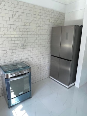 A kitchen with white marble tiles, a stainless steel double-door refrigerator, and a glass-top stove. - Kingdom Rentals - AirBnCar (Loubiere)