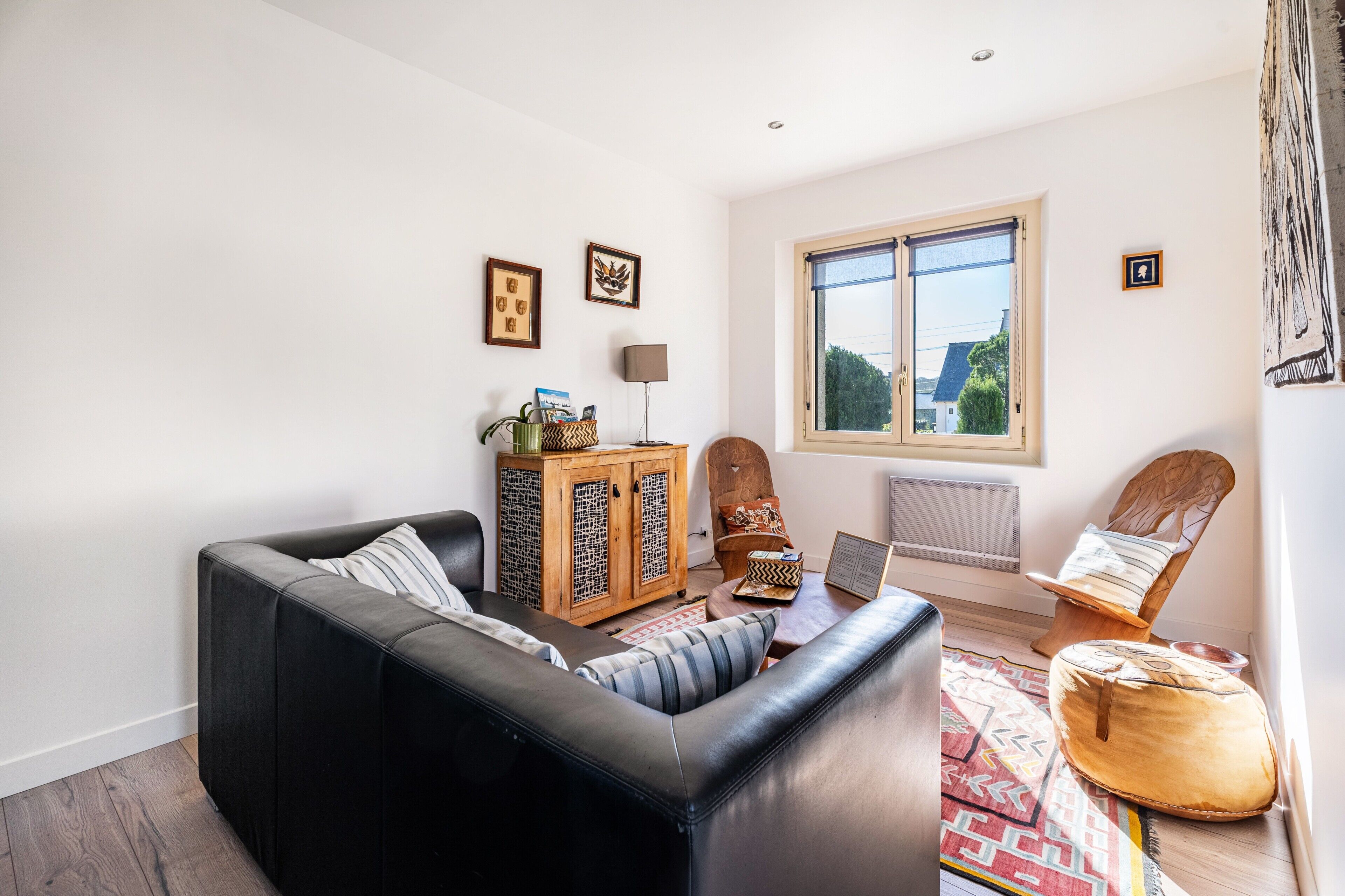 A living room with a black sofa, wooden cabinet, and a window with a view.