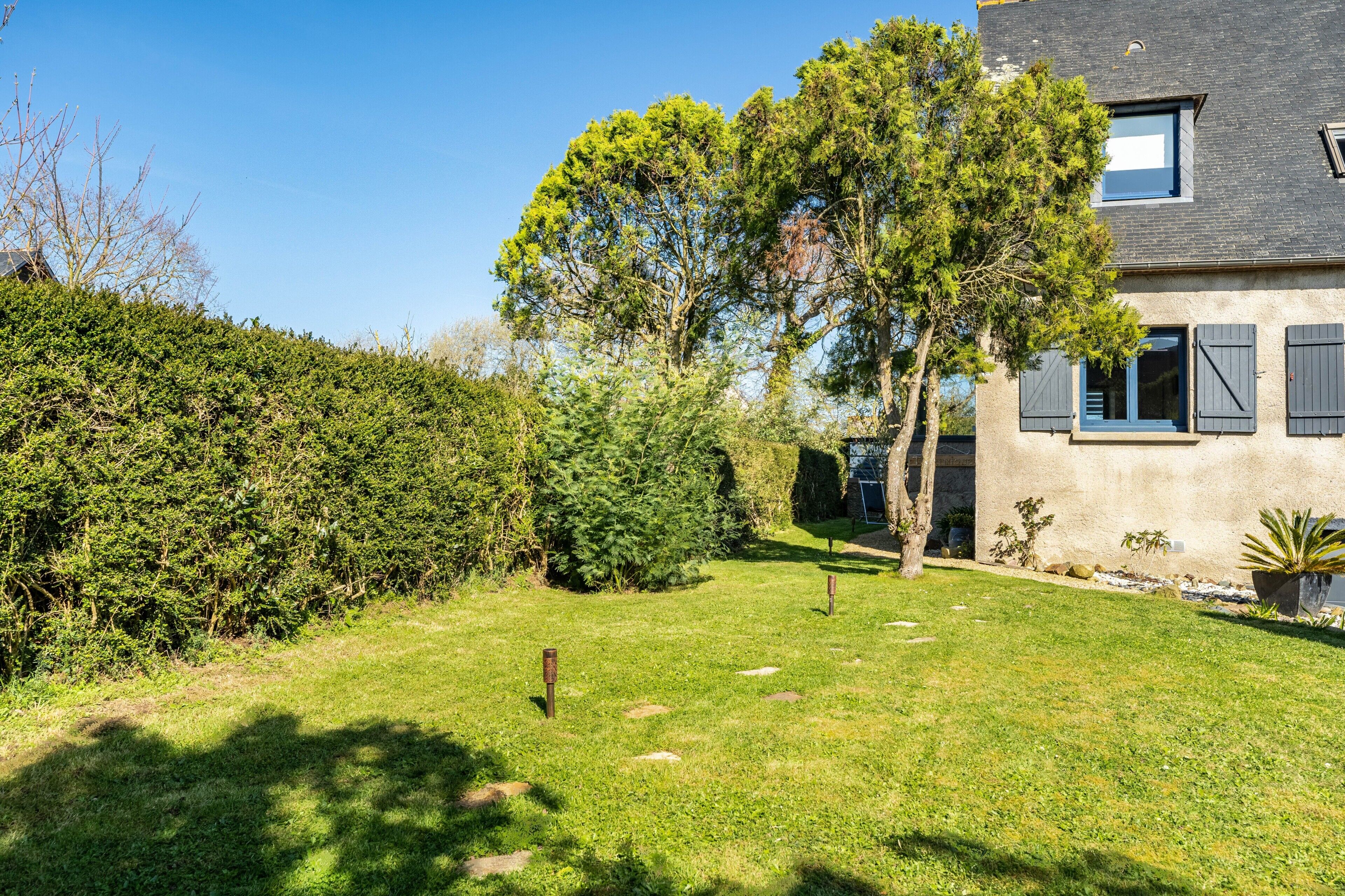 Ein Haus mit gepflegtem Rasen, einem großen Baum und einer Hecke.