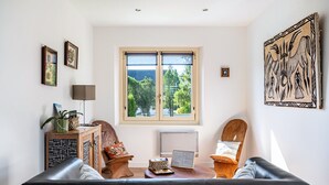 Een woonkamer met een bank, een bijzettafeltje, een radiator en een raam met uitzicht op bomen.