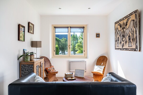 Een woonkamer met een bank, een bijzettafeltje, een radiator en een raam met uitzicht op bomen.