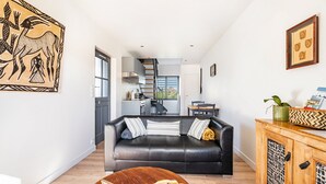 Een moderne woonkamer met een zwarte leren bank, een houten salontafel en een trap die naar een verdieping leidt.