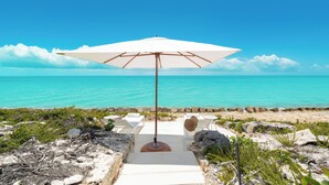 Uitzicht op het strand met een witte parasol, een pad van stenen en een rotsachtige kustlijn.