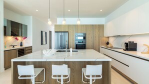 Een moderne keuken met een centraal eiland, barkrukken, houten kastjes, roestvrijstalen apparatuur en hanglampen.